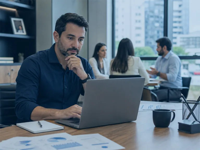 Gestor brasileiro em ambiente corporativo realista, analisando relatórios de vendas, estoque e financeiro em notebook sobre mesa organizada, com equipe ao fundo em reunião, iluminação natural, estilo profissional e humano, sem dados legíveis na tela