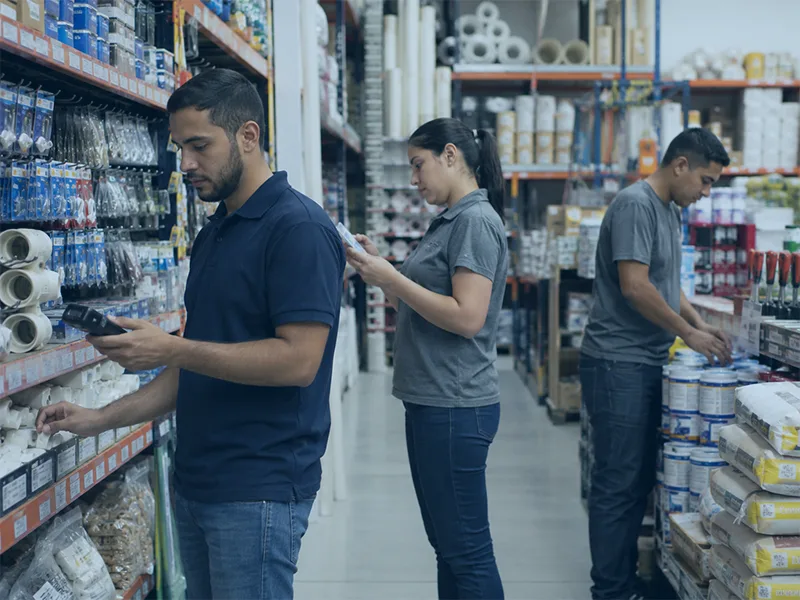 Three people are standing in a store aisle, examining products on shelves.