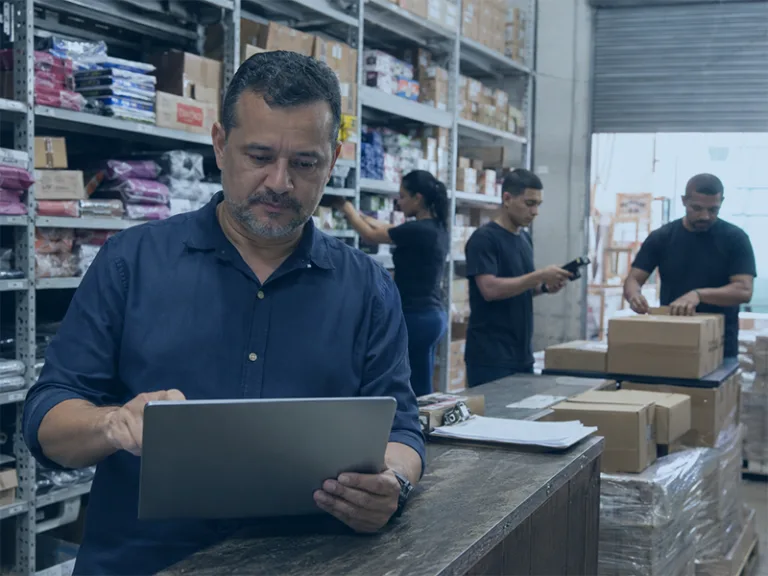 Gestor acompanha indicadores para distribuidoras enquanto colaboradores separam e conferem mercadorias