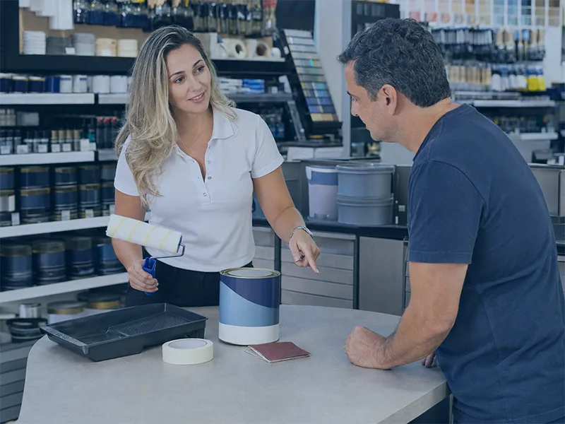 Vendedora orientando cliente sobre venda adicional em loja de tintas